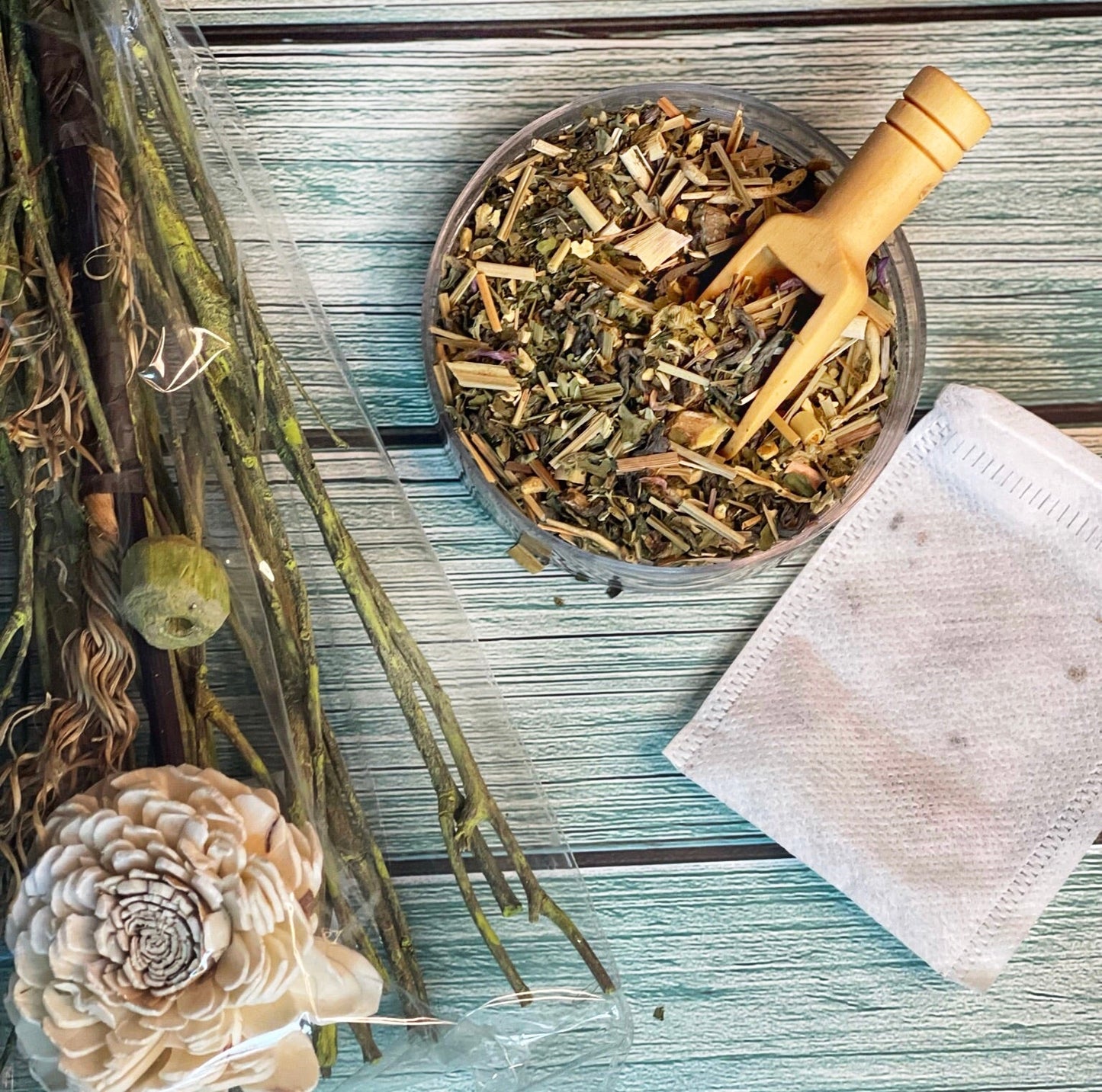 Flat-lay of Detox Tea blend showcasing a bowl of loose-leaf tea accompanied by a tea bag and decorative elements on a turquoise wooden background, highlighting a blend crafted to support the body’s natural detoxification process and promote wellness, as described on the product page.