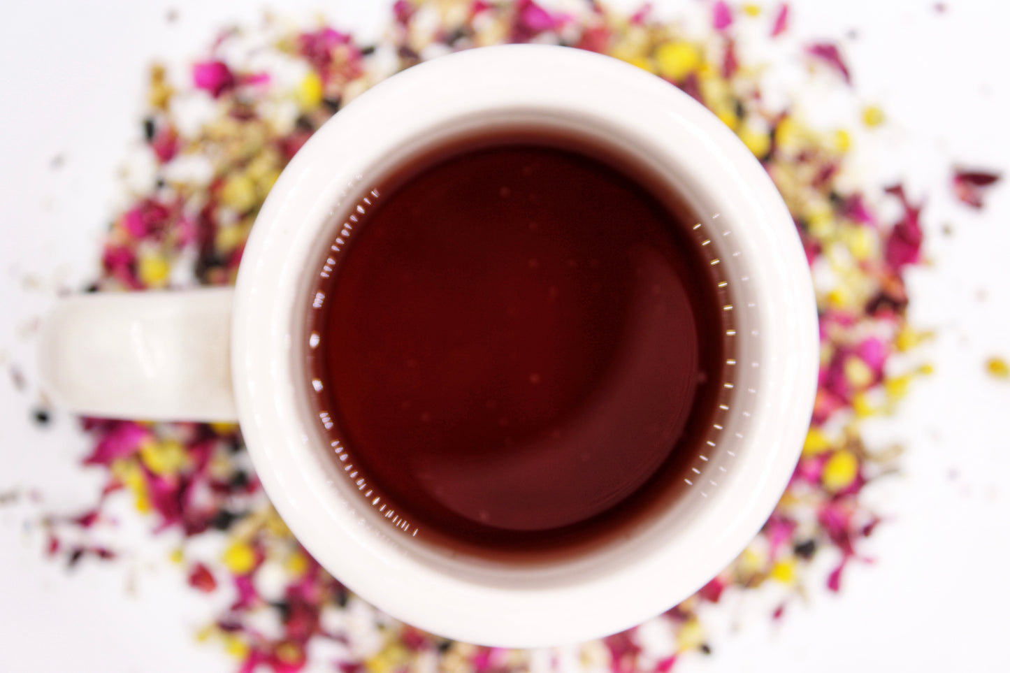 Top-down view of a steaming cup of Breathe Easy Tea surrounded by its natural loose-leaf blend, featuring chamomile, rose petals, elderberries, and a soothing herbal medley designed to promote relaxation and respiratory comfort, showcasing the tea’s vibrant colors and calming benefits.