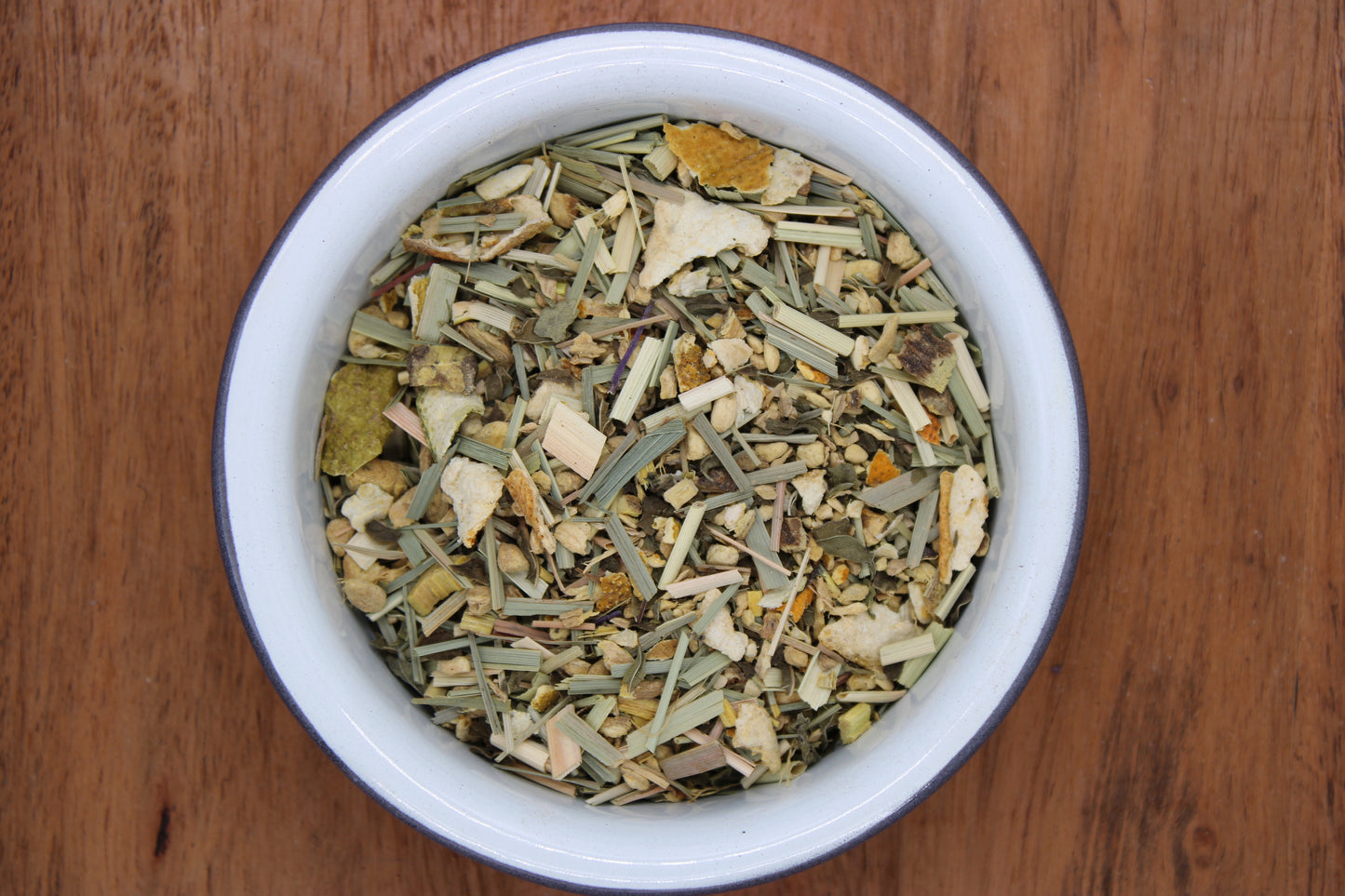 Top-down view of Organic Lemon Ginger Tea blend by Relaxation Tea in a white bowl on a wooden surface, showcasing its vibrant ingredients including organic ginger, lemongrass, lemon peel, licorice root, and spearmint. This refreshing and zesty blend is designed to support digestion and relaxation, highlighting Relaxation Tea’s commitment to organic, high-quality wellness teas.